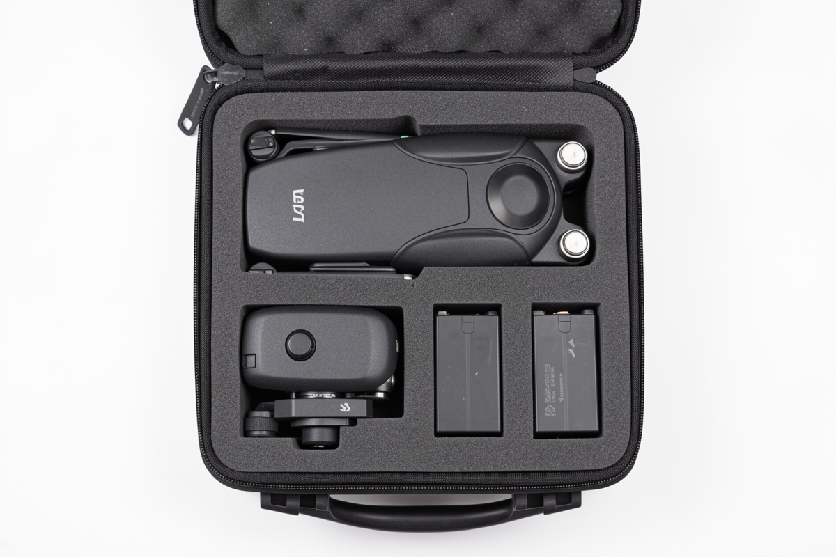 An open compact drone travel case showing the folded drone, controller and spare batteries in foam cutouts