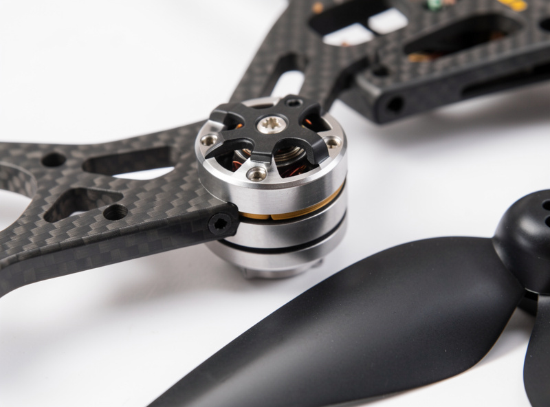 Close-up of a 2207 brushless motor being bolted to a carbon FPV frame arm with a tri-blade 5-inch propeller beside it