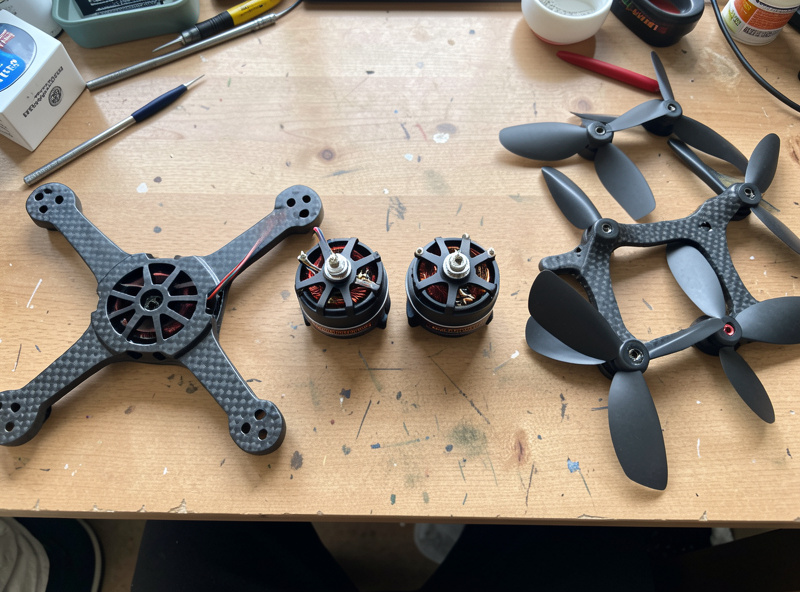 Four FPV brushless motors laid out on a soldering bench next to a quad frame and props