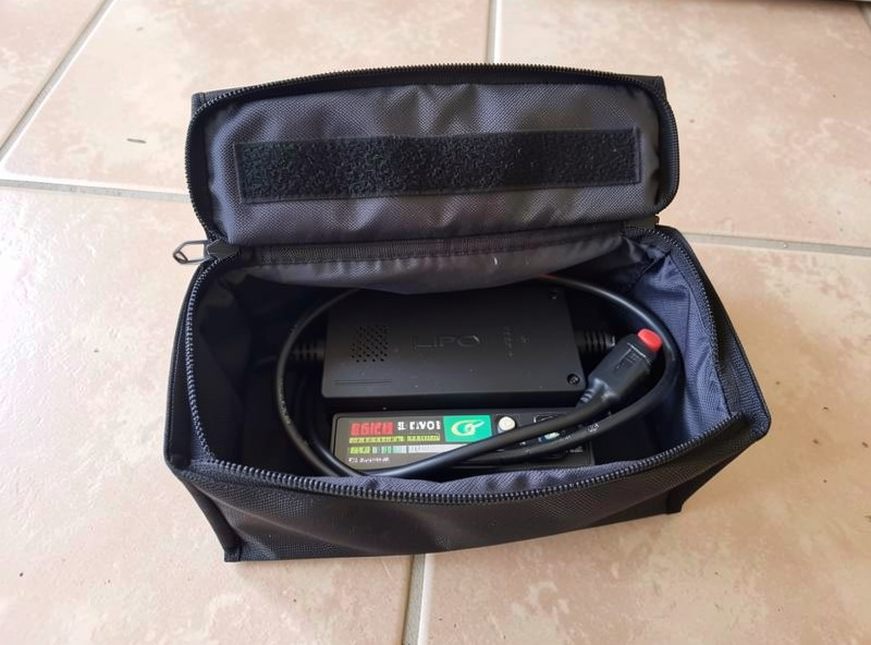 An open fire-resistant LiPo charging bag on a tile floor with a battery pack and charging lead inside