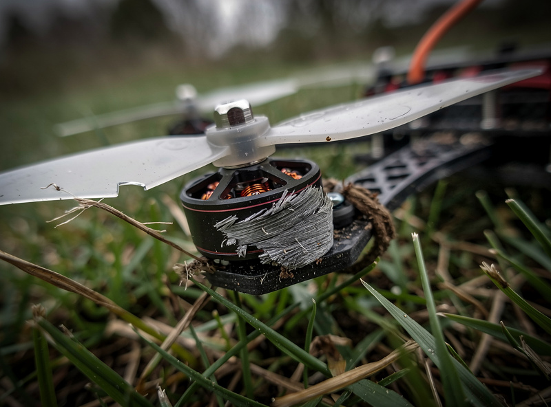 A crashed FPV drone with a broken propeller lying in grass, illustrating the cost of beginner mistakes